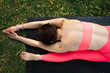 Top view on the back of  streching caucasian girl wearing in a pink top and leggins on the black mat outside