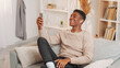 © golubovy - Phone video chat. Internet call. Joyful smiling man in wire earphones talking on mobile cell online web meeting on couch at home in living room.