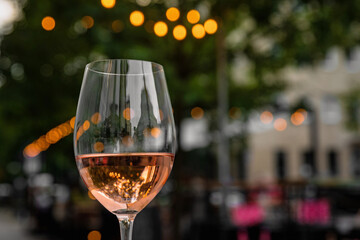 Glass of refreshing rose wine on a table of a city cafe terrace on summer evening. Street in bokeh.