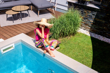 Wall Mural - Happy woman wearing beachwear and sunglasses while relaxing by the poolside