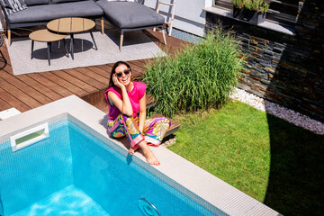 Happy woman wearing beach wear and sunglasses while relaxing by the poolside