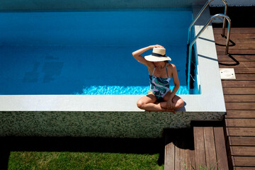 Wall Mural - Full length shot of an attractive woman wearing swimsuit and sunhat while relaxing by the swimming pool