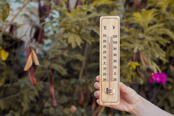 Fototapete - Hot weather. Thermometer in hand in front of green plants during heatwave. High temperature concept