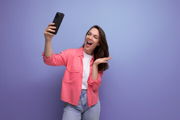 modern brunette woman in pink shirt broadcasting video using phone on studio background