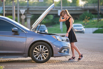 Wall Mural - Helpless woman standing near her car with open bonnet inspecting broken motor. Young female driver having trouble with vehicle