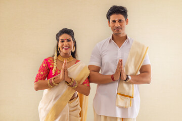 Wall Mural - South Indian couple in traditional clothing greeting on the occasion of Onam against white background