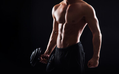 Wall Mural - Strong, fit and sporty bodybuilder man with a dumbbell over black background