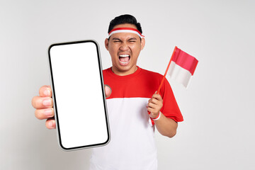 Excited young Asian men celebrate Indonesian independence day on 17 August while holding smartphone with blank screen and Indonesian flag isolated over white background