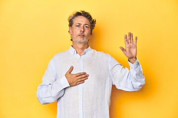 Wall Mural - Middle-aged man posing on a yellow backdrop taking an oath, putting hand on chest.