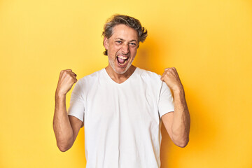 Wall Mural - Middle-aged man posing on a yellow backdrop cheering carefree and excited. Victory concept.