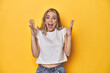 © Asier - Young blonde Caucasian woman in a white t-shirt on a yellow studio background, celebrating a victory or success, he is surprised and shocked.