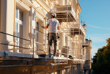 Renovation, Restoration, Refurbishment. Unrecognizable Worker Renovating Wall Of Classical Style Building, Standing On Scaffolding. Construction Worker Prepares House Facade Wall For Painting Outdoors