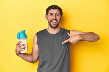 Fit man with protein shake, yellow studio background person pointing by hand to a shirt copy space, proud and confident