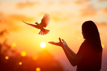  Silhouette hand of woman praying and free bird enjoying nature on sunrise and orange background with sunlight.