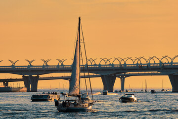 Sailing yacht leaves the bay into the sea at sunset. A sailboat in backlight floats across the bay among motor boats and passenger ships.