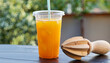 disposable plastic glass of cold freshly squeezed orange juice with wooden juicer on table outdoors. Fresh drink concept