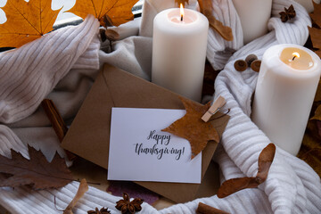 HAPPY THANKSGIVING text greeting card concept Celebrating autumn holidays at cozy home on the windowsill Hygge aesthetic atmosphere Autumn leaves spices and candle on knitted white sweater in warm