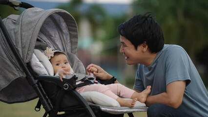 Wall Mural - happy father talking and playing with his infant baby in the stroller while resting in the park