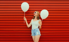 Happy Cheerful Young Woman Having Fun With Balloon Wearing White Heart Shaped Sunglasses, Shorts On Red Background