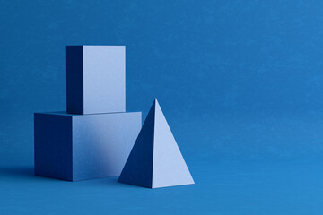 Three-dimensional prism pyramid and rectangular cube objects on blue colored background.