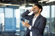 © Liubomir - Upset and disappointed man reading online bad news using app on smartphone, depressed businessman at workplace standing near window inside office with phone, arab boss in business suit.