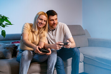 Happy young Caucasian couple playing video gam console at home, happy and affectionate 