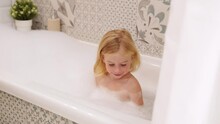 Adorable Caucasian Three Years Old Gir With Curly Hair Taking Bath With White Foam Bubbles, Playing,laughing,having Fun.Carefree Childhood, Kid Body Care And Hygiene Concept.
