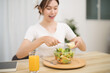 © Charlie's - Happy beautiful Asian woman eating healthy food with vegan.salad in the kitchen at home.