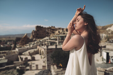 Wall Mural - A girl in a flying dress on the roof of a house on ancient city background.