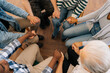 © dikushin - Closeup top view of unrecognizable multicultural and different ages people holding each others hands sitting in circle, support each other, during group psychotherapy session. Concept of mental health