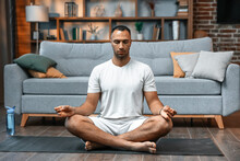 Young Man Meditating On His Living Room Floor Sitting In The Lotus Position With His Eyes Closed And An Expression Of Tranquility In A Health And Fitness Concept