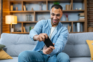 Young man playing video game on his smartphone winning a racing game in living room. Mobile application concept