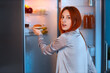 © Pixel-Shot - Young woman taking tasty burger from fridge in kitchen at night