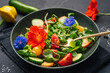 Green salad with cucumbers, tomato, peach and nasturtium flowers on black background