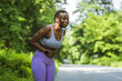 Shot of an young African woman experiencing stomach ache while working out in nature.