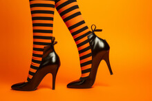 Close Up Of Witches Legs Wearing Orange And Black Striped Tights Against An Orange Background