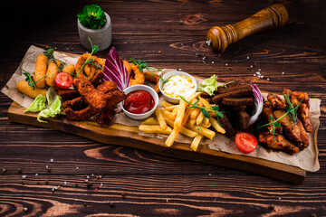 Wall Mural - Snacks chicken wings, French fries, rye bread croutons, breaded squid rings, mozzarella cheese sticks with greens and sauces.