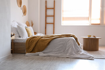 Poster - Cozy bed with white blanket and coffee table in interior of light bedroom