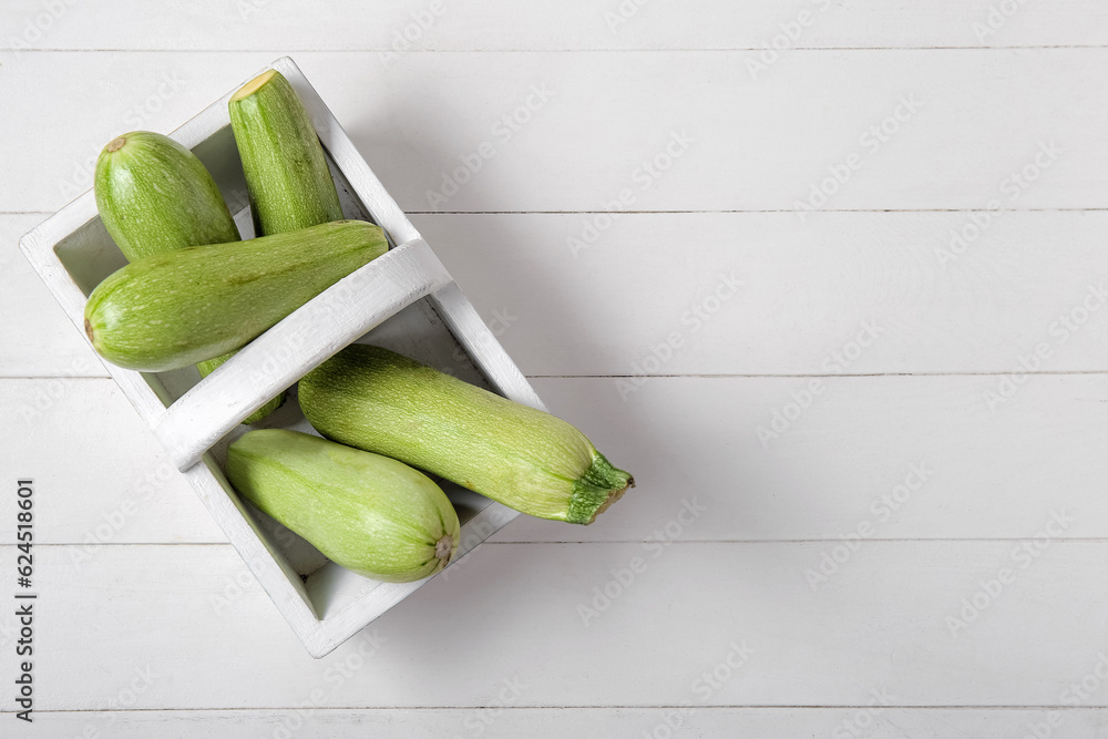 Basket with fresh green zucchini on white wooden background