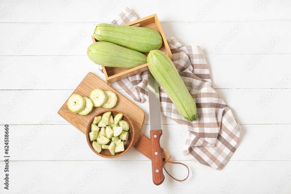 Board and box with fresh green zucchini on white wooden background