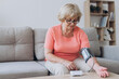 © anatoliycherkas - Senior woman with hypertension measuring blood pressure herself at home. Sad Mature lady measure blood pressure using tonometer. Everyday health check-up