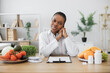 Charming african american lady in lab coat looking at camera while working in professional office of dietitian. Happy nutrition expert helping people lead healthy lifestyles by giving advice on food.