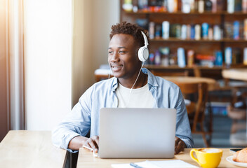African American man with laptop, headset enjoying music in cafe