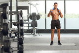Fototapeta Panele - Young fit man with a towel around his neck standing at a gym