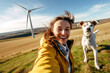 Smiling young attractive woman and her dog takes a selfie against the backdrop of a nature landscape with wind turbines. The concept of ecology, sustainable resources and climate optimism