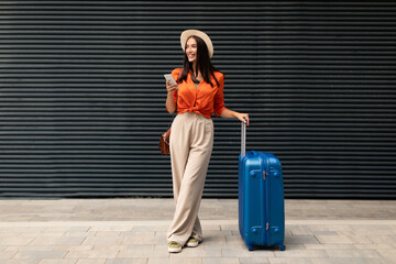 Cheerful Passenger Woman With Travel Suitcase Using Smartphone Standing Outdoors