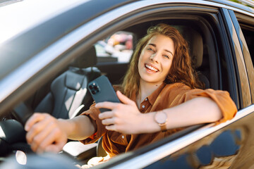 happy woman in the car in the driver's seat looks at the smartphone. a young woman uses a mobile pho
