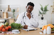 © sofiko14 - Doctor gastroenterologist filling patient's case history and prescribing recipe wile sitting at work desk full of fruits and vegetables. Male professional writing vegetable diet plan in clinics.