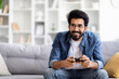 © Prostock-studio - Domestic Entertainment. Smiling Young Indian Man Playing Video Games At Home