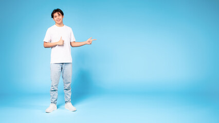 Wall Mural - Chinese guy pointing aside gesturing thumbs up on blue background